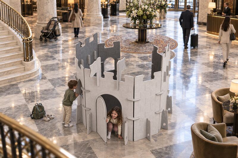 Two children playing in a grey Castle XL play-screen in a hotel lobby
